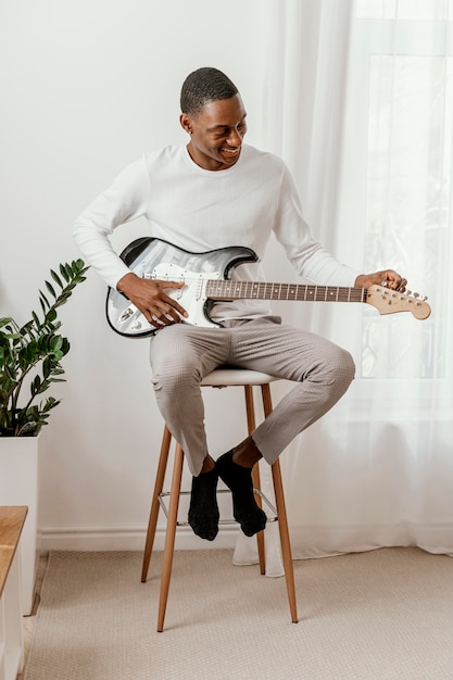 自宅でエレキギターを弾く笑顔の男性ミュージシャンの正面図
