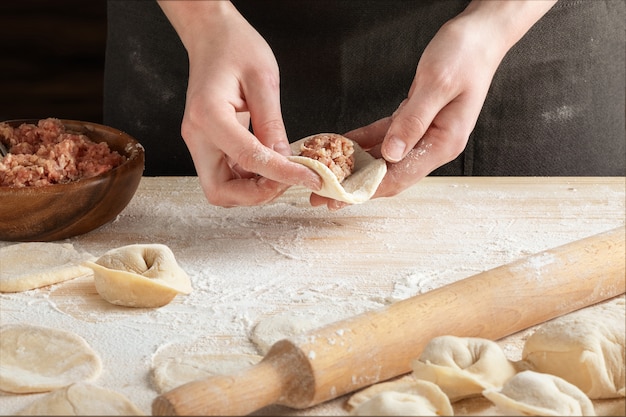 写真 木製麺棒で肉団子を作る女性の手の正面図。