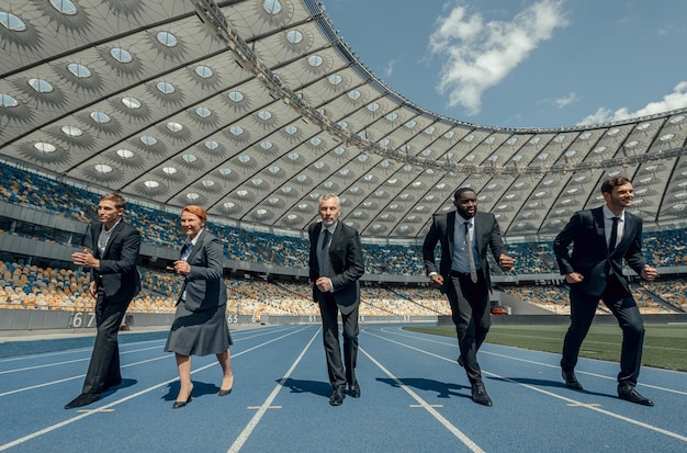 Vista frontale di persone vestite con abiti da lavoro che corrono su una moderna pista sportiva allo stadio