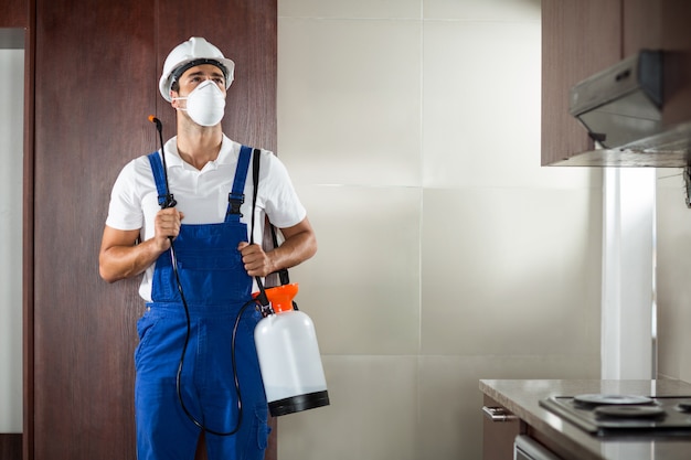 Front view of pest worker spraying in kitchen