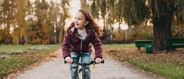 Front view photo of a caucasian girl riding the bike in the park while looking at her parents