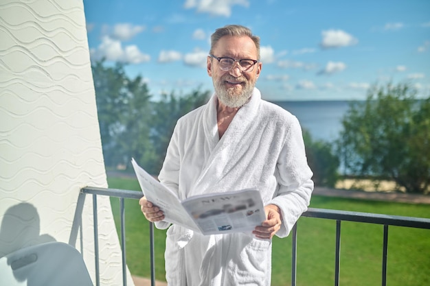 Front view of a pleased man in eyeglasses posing for the camera leaned on the balcony railing