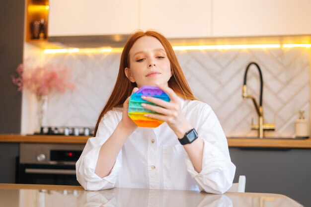 Front view portrait of attractive redhead young woman playing fidget toy new trendy silicone toy