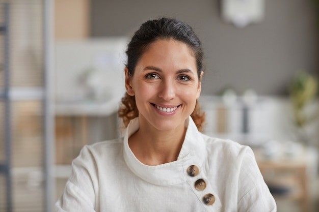 Front view portrait of beautiful adult woman smiling at camera while working in office, copy space