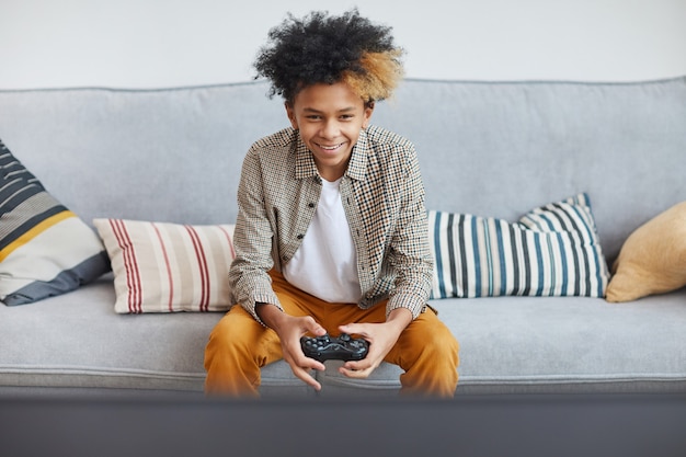 Front view portrait of excited African-American boy playing video games at home and holding gamepad, copy space