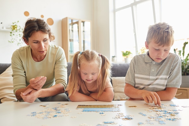 Ritratto di vista frontale della famiglia amorevole con bisogni speciali bambino che gioca con i puzzle e giochi da tavolo insieme a casa, copia dello spazio