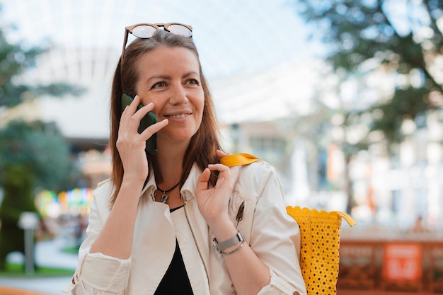 Photo front view portrait modern fashion happy woman hipster walking and using a smart phone on a city street wearing sunglasses in the summer sun