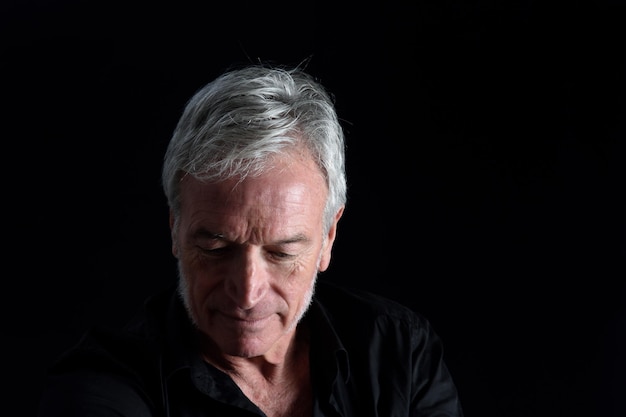 Front view portrait of senior man looking down on black background