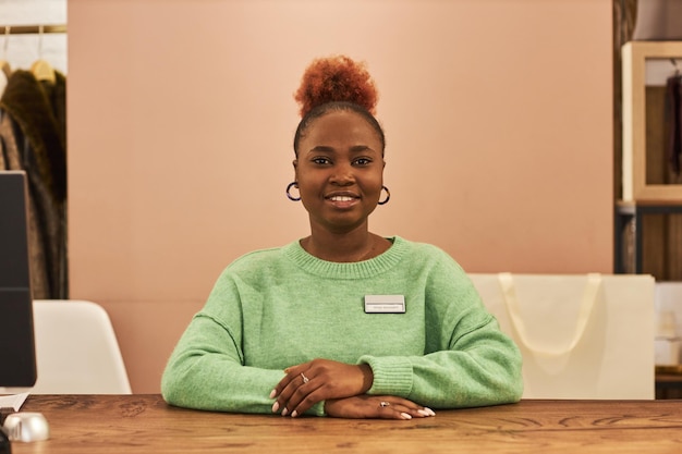 Front view portrait of smiling black woman looking at camera at counter working in clothing store copy space