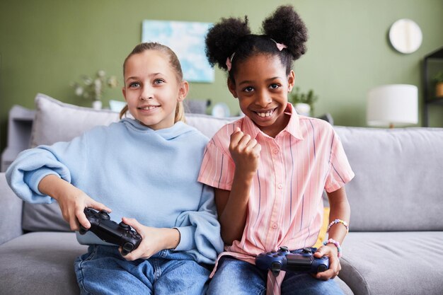 Портрет двух девушек, вид спереди, играющих в видеоигры дома и развлекающихся в помещении, копируя пространство