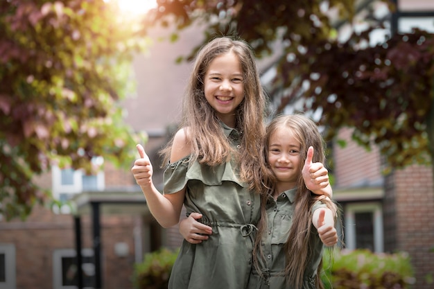 Front view portret of two funny sisters with thumbs up and looking to the camera