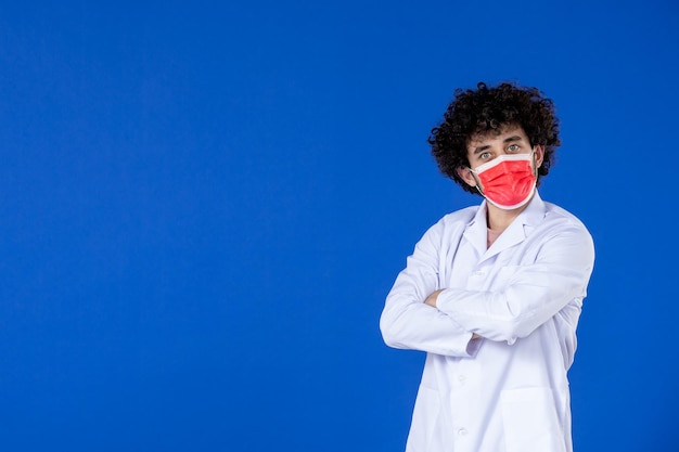Vista frontale del medico maschio in posa in tuta medica e maschera su sfondo blu vaccino ospedale covid medicina virus farmaco salute pandemia coronavirus Foto Premium