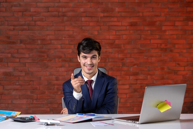 front view of posing travel agent sitting behind his working place in suit corporate tourism occupation agency assistant project global service