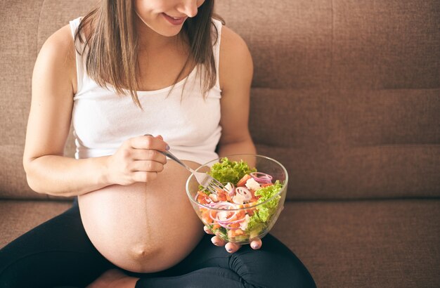 Front view of pregnant woman eating fresh salad at home