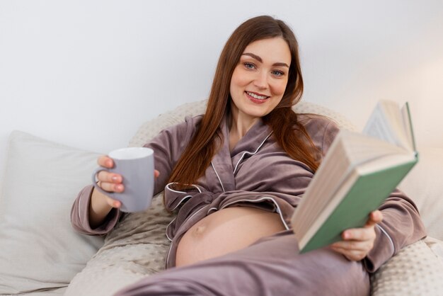 Foto lettura della donna incinta di vista frontale a letto