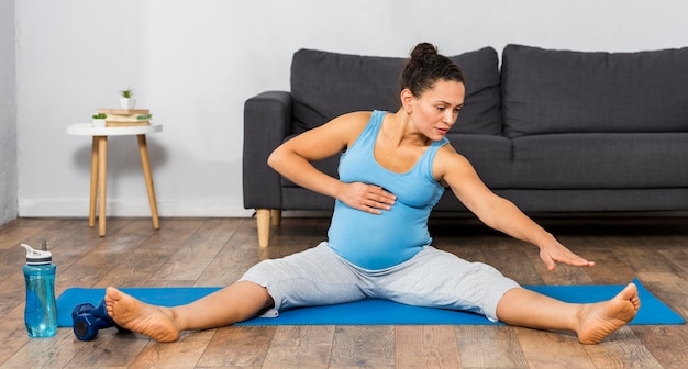Photo front view of pregnant woman training at home on mat
