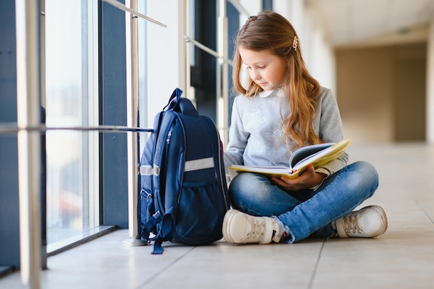 多くのカラフルなメモや本を持っているかわいい金髪の女子高生の正面図インターナショナルスクールの廊下に立っているカメラに微笑んでいる賢い十代の少女