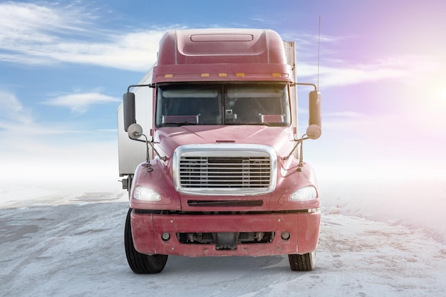 Front view of red long distance bonnet truck with a white semitrailer on bright background with sky