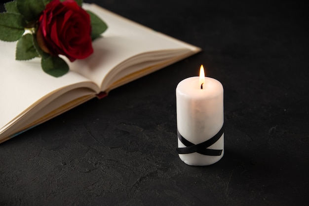 Vista frontale della rosa rossa con libro e candela su nero