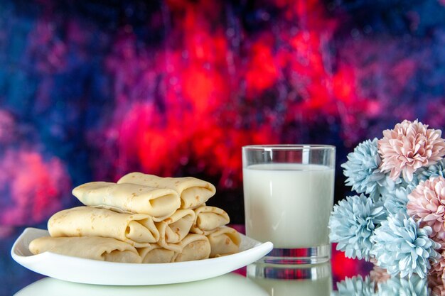Vista frontale dolci arrotolati frittelle con un bicchiere di latte su sfondo scuro pasto colazione cibo fiore torta di colore torta del mattino