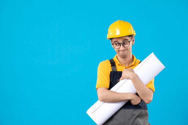 Vista frontale del costruttore maschio triste in uniforme gialla con piano blu