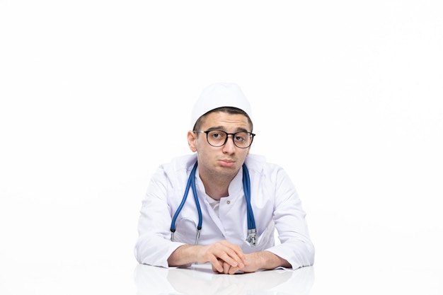 Front view sad male doctor in medical suit sitting behind desk