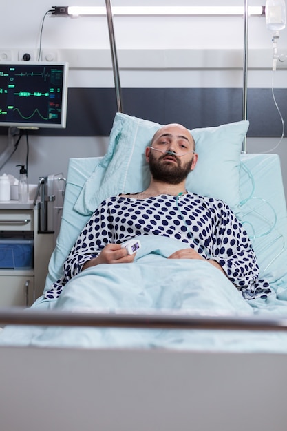 Front view of sad sick man with nasal oxygen tube having respiratory disease resting in bed during therapy treatment