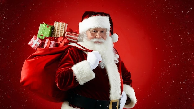 Front view santa claus carrying red bag full of presents on a red christmas emotion new year holida