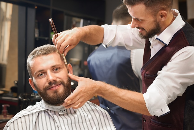 Vista frontale del maschio soddisfatto nel negozio di barbiere che ottiene taglio di capelli