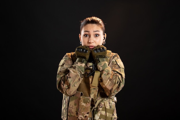 Front view of scared female soldier in camouflage on a black wall