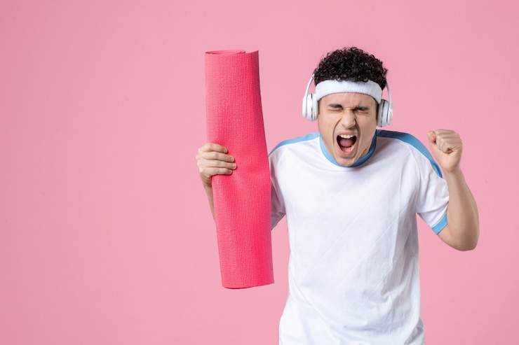 Photo front view screaming young male in sport clothes with yoga mat and headphones
