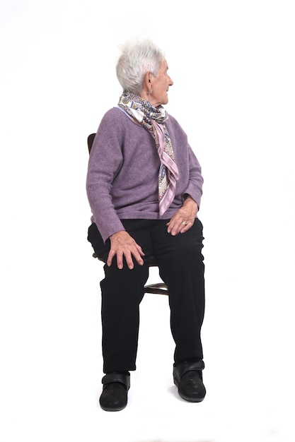 Front view of a senior woman sitting on chair and looking back on white background