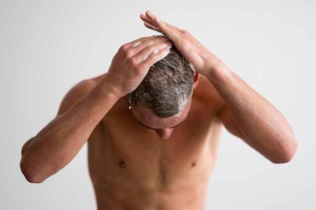 Vista frontale dell'uomo senza camicia che lava i suoi capelli con lo shampoo