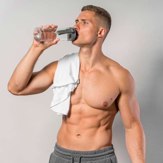 Photo front view of shirtless man with towel drinking water