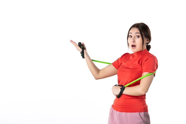 Front view of a shocked young woman neatly gathering her hair dressed in redorange blouse and holding rope sport accessory pointing up on white background