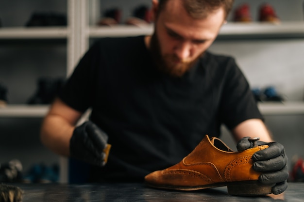 Front view of shoemaker wearing black latex gloves polishing old light brown leather shoes for later...