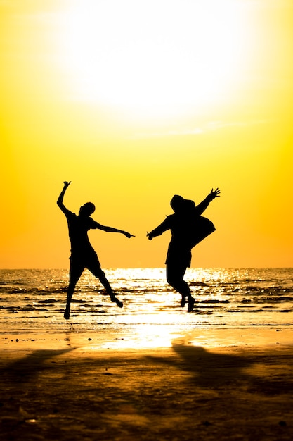 Front view of silhouette young man and young girl jumping over the sea beach with sunset background.