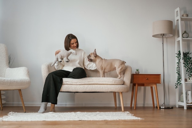 小さなソファに座っている前向きの景色 若い女性はパグ犬と一緒に家にいる