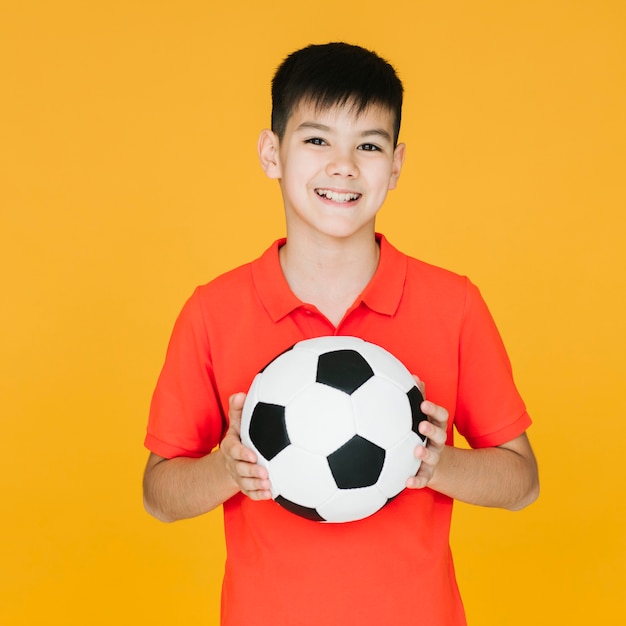 Photo front view smiley kid holding a football ball