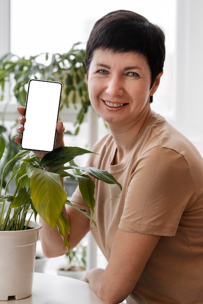 屋内植物の横にスマートフォンを持っている笑顔の女性の正面図