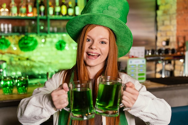 Front view of smiley woman with hat celebrating st. patrick's day at the bar