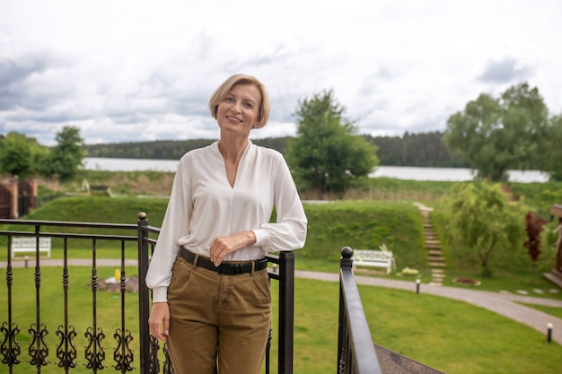 Front view of a smiling contented mature woman standing by the wrought-iron railing on the terrace