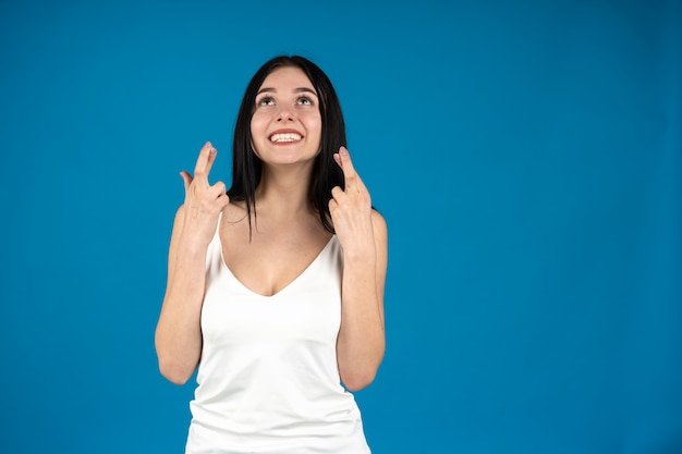 Foto vista frontale della ragazza sorridente con le dita incrociate isolate sul blu