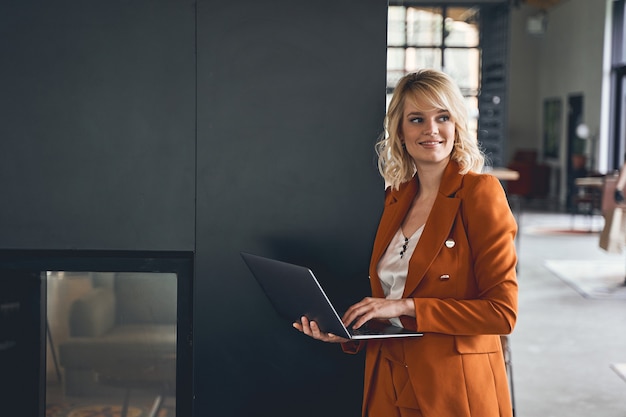 Front view of a smiling relaxed female freelancer with a laptop in her hand looking away