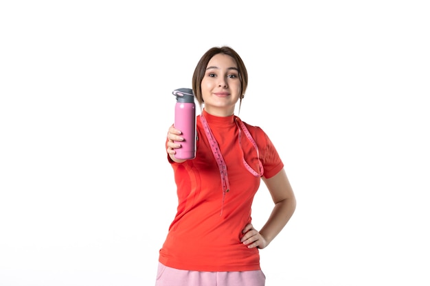 Front view of a smiling young girl in redorange blouse holding metre and showing thermos on white background