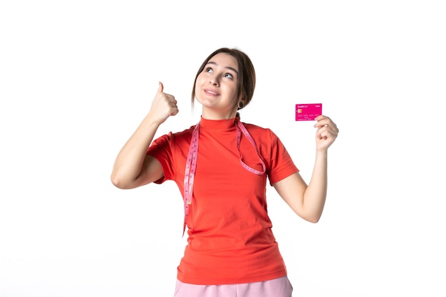 Front view of smiling young girl in redorange blouse showing bank card pointing up on white background