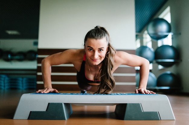 Front View sporty girl doing push-ups on step platform, aerobics in gym