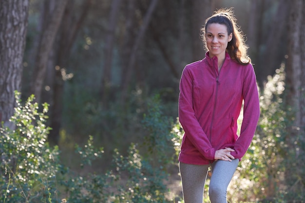 Front view sporty woman stretching while smiling through the forest