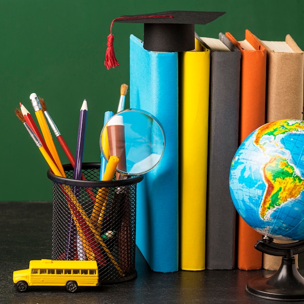 Front view of stack of books with academic cap and globe