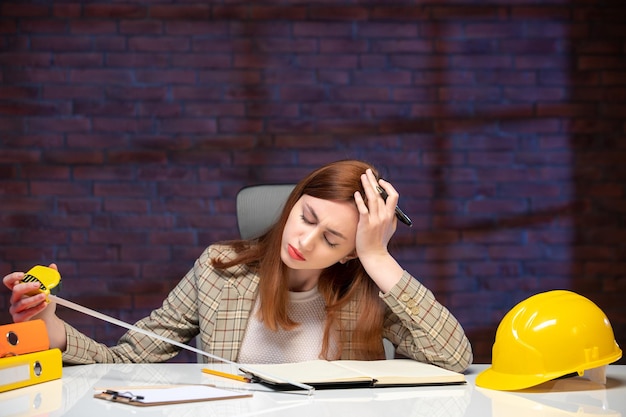 front view stressed female worker in construction site holding tape measure and writing notes agenda engineer corporate project business job plan manager